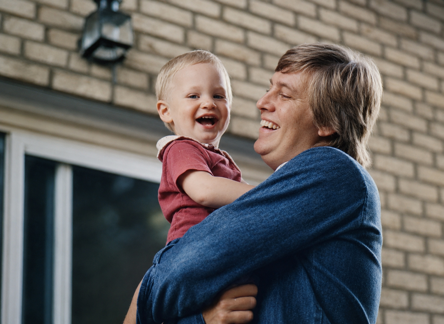 Dave laughing while holding his young son outside the family home